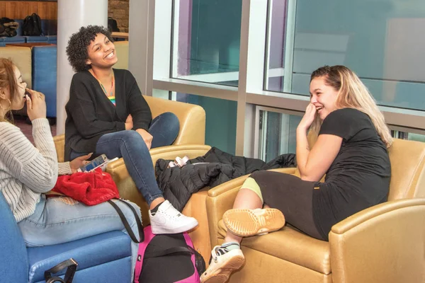 A group of three students relax in a campus lounge, smiling and laughing.
