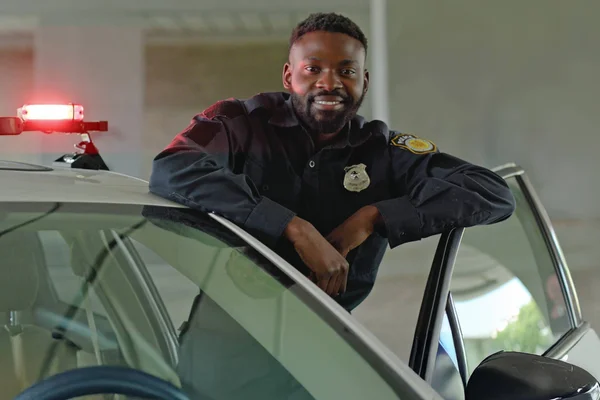 A police officer leans casually against the open door of his squad car, posing for a portrait.