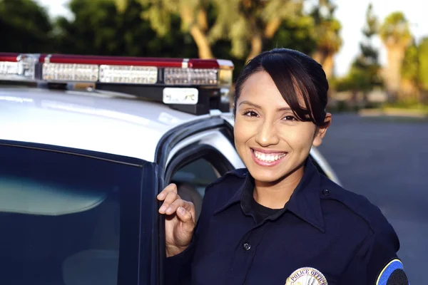 A police officer leaning against the side of a patrol car, smiling, and looking directly at the camera.