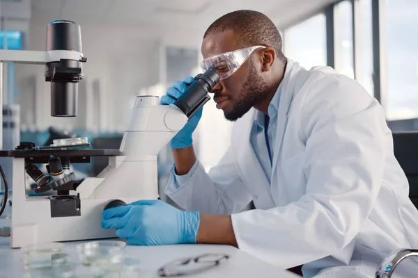 Lab tech looks at a slide through a microscope in the workplace.