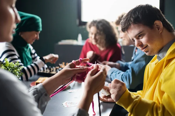 Direct Support Professionals and their clients gathered around a table, knitting, and playing chess.