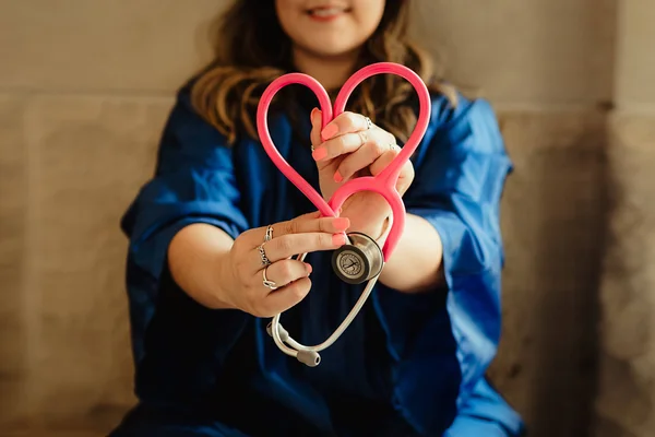 A medical professional holding a stethoscope in the shape of a heart.