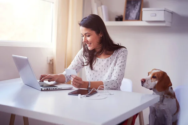 A student using a laptop computer to participate in an online class. A dog sits nearby.