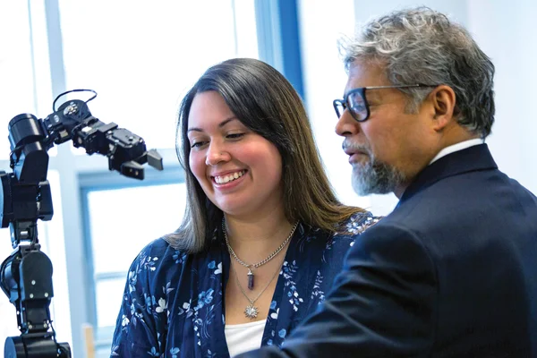 Student and FLCC faculty member work together with a robotic arm.