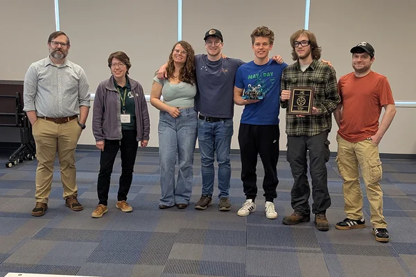 Seven people standing in a row, one holding a plaque