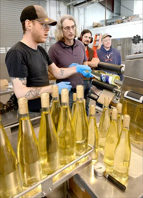 Instructor with students monitoring wine labeling machine with filled bottles in the forefront