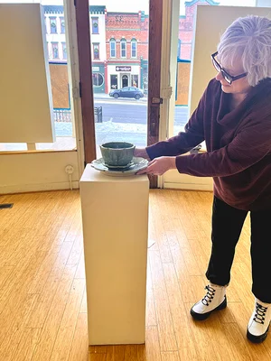 Woman positions ceramic bowl on pedestal in art gallery