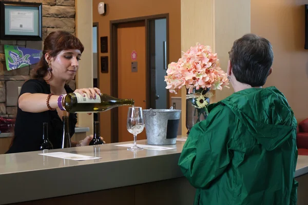 A woman serves a glass of wine to an event attendee.