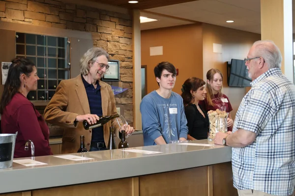 Group of 5 individuals communicating and serving an event attendee wine.