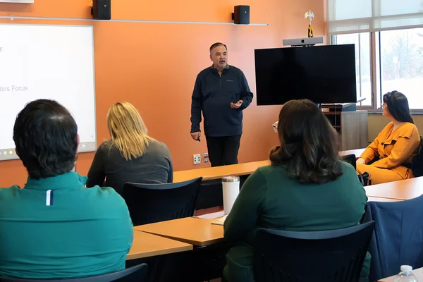 A man standing and speaking to others seated in a classroom