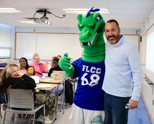Flick poses with a faculty member while students observe and laugh.