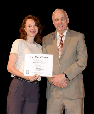 A woman holding an honor society certificate poses with a man in a suit