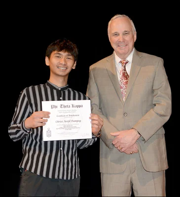 A young man holds up and honor society certificate posing with an older man in a suit