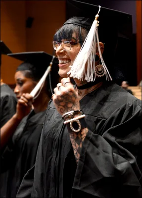 A woman in black cap and gown smiles and clenches fists in celebration
