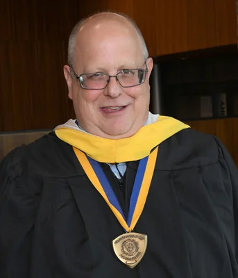 Head and shoulders photo of man in academic regalia wearing a medal