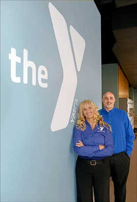 A woman and man standing next to a wall painted with the YMCA logo